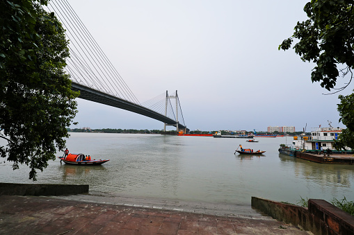 Kolkata WB India - May 4, 2022 : Picture of Rabindra Setu; the howrah bridge in KOlkata at sunset. There is a tour boat sailing in front giving joy ride to tourists.