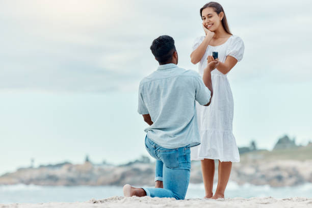 beach proposal, engagement and surprise woman for love, care and relationship commitment together. young, engaged and happy marry me couple, summer seaside date and special romance marriage outdoors - fästfolk bildbanksfoton och bilder