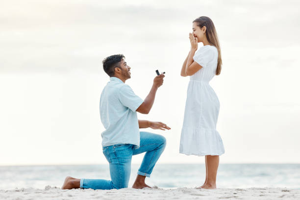 engagement, beach and a couple with a marriage proposal with a ring while on romantic vacation. love, romance and happy couple getting engaged while on a summer holiday in nature by the ocean. - wedding ring love engagement imagens e fotografias de stock