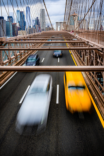 Moving taxi and other cars on Brooklyn bridge with the downtown of New York City in the background.