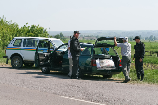 Ukraine, May 27, 2011. Officers inspecting the trunk of a car. The driver is watching.
