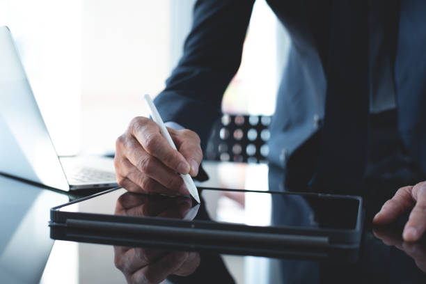 istock Businessman using stylus pen signing e-document on digital tablet with laptop computer on table at office, e-signing, electronic signature, paperless office 1442933626