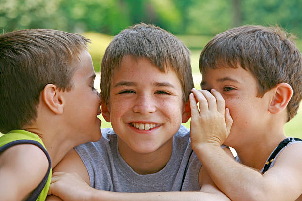 istock Two young boys whisper into another smiling boy's ears 144293464