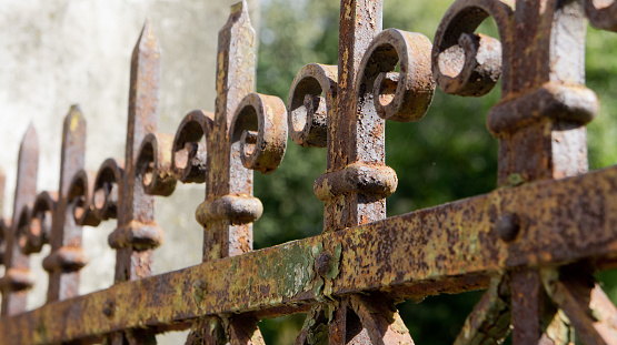 A rusted, decorated, wrought iron fence. Detail of an old retro iron fence made with decorated ironwork elements. Old and worn, still showing some of its former splendor