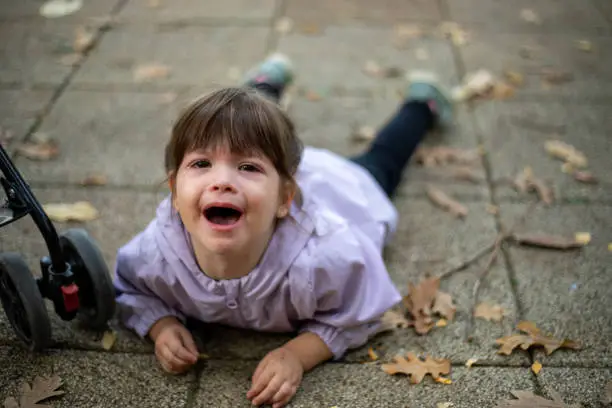 Photo of A little girl is lying on the ground in a public park and crying.