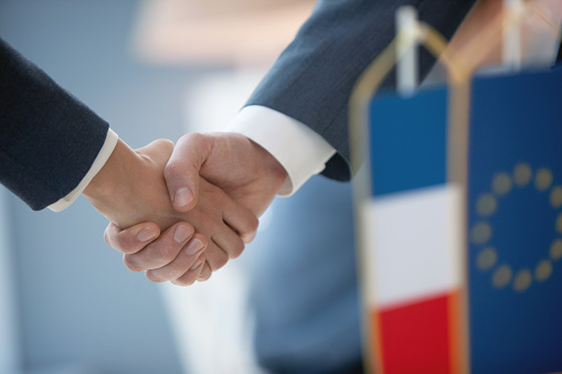 Officials of foreign countries shaking hands, French and EU flags up front