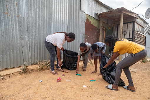 Volunteer Worker showing teenage girls to pick up garbage in their community.  They are holding black rubbish bags and are putting the trash rubbish inside.