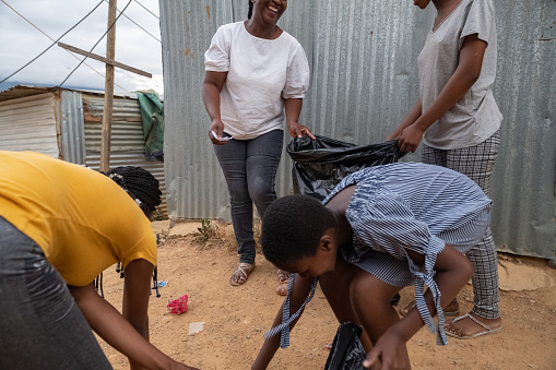 Happy Volunteer Worker showing teenage girls to pick up garbage in their community.  They are holding black rubbish bags and are putting the trash rubbish inside.