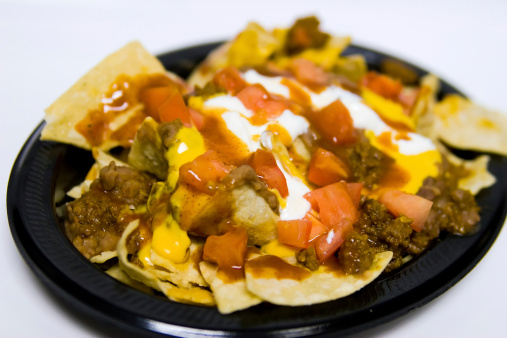 Big serving of mexican nachos on a plate with meat, cheese, tomatoes, sour cream, and chips