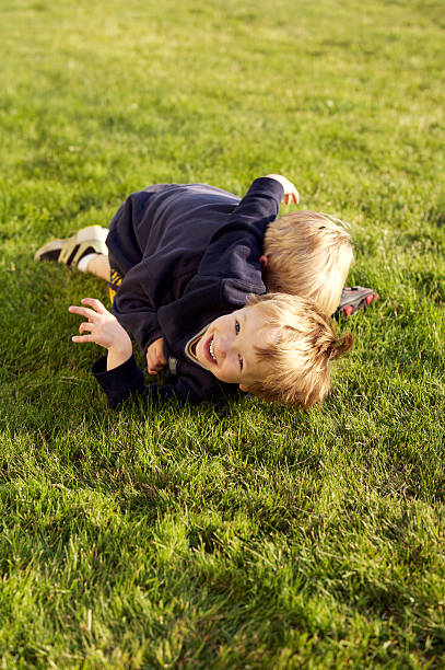 Three little boys play fighting in the park.