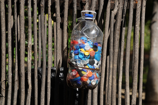 Bottles cups to recycle. Big plastic gallon full of colored bottles cups sunny day hanging on a fence