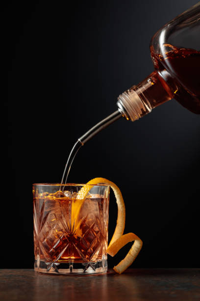 whiskey is poured into a glass with ice and orange peel. - action alcohol alcoholism bar imagens e fotografias de stock