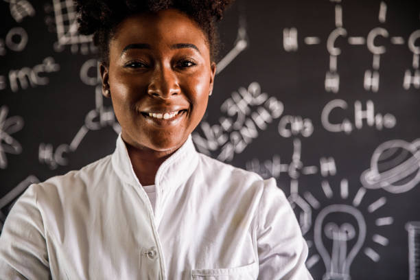 chemistry technician standing in front of a blackboard with formulas and confidently smiling at camera - professor scientist chemistry teacher imagens e fotografias de stock