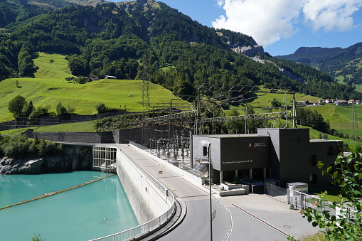 Hydroelectric power plant with three turbines on reservoir Mapraggsee. The power plant belongs to company called Kraftwerke Sarganserland AG. Behind are mountains.