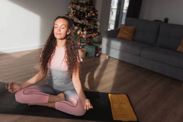 Woman meditating by a Christmas tree Fit woman sitting in front of a Christmas tree and meditating Mental Strength and Resilience: stock pictures, royalty-free photos & images