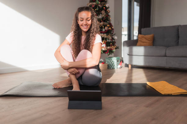 Fit woman sitting on a yoga mat and smiling when looking at digital tablet stock photo