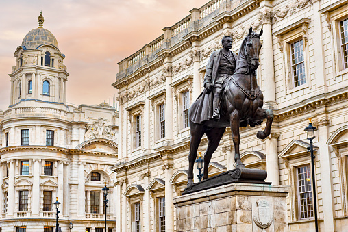 A statue with a man on horseback sits in central London with buildings in its background