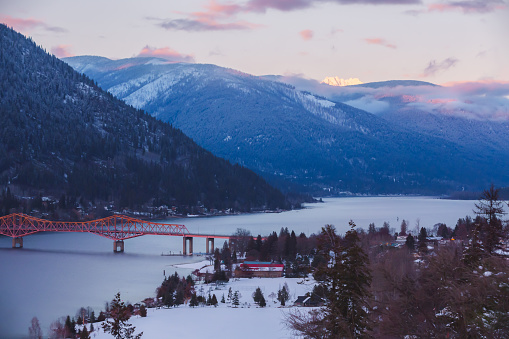 Winter view from Gyro Park of the big orange bridge across the west arm of Kootenay Lake and the snowcapped peak of Kokanee Glacier mountain catching sunset light in Nelson, BC, Canada.