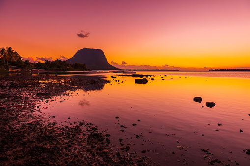 Quiet ocean at low tide and colorful sunset time. Le Morn mountain in Mauritius.