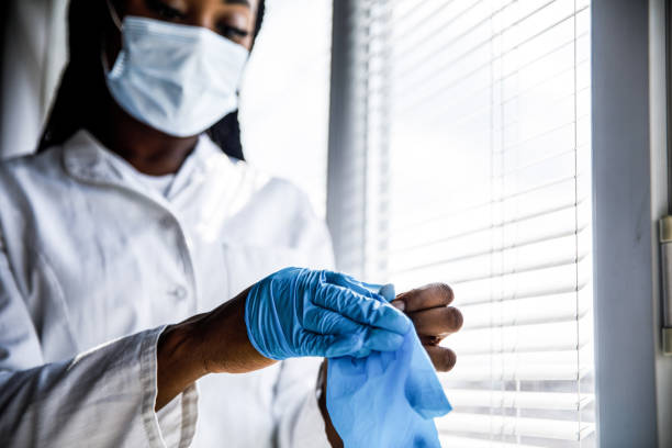 istock Female scientist standing by the window, taking off protective gloves while catching a small break from work 1442967859
