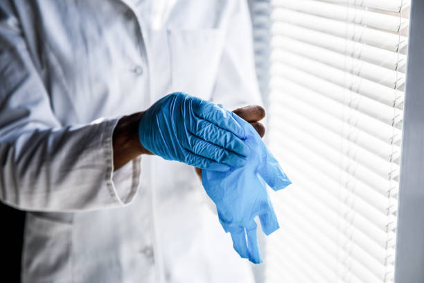 Female scientist standing by the window, taking off protective gloves while catching a small break from work Close up shot of unrecognizable young female scientist standing by the window, taking off protective gloves while catching a small break from doing experiments at the laboratory. putting on latex gloves stock pictures, royalty-free photos & images