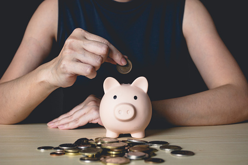 Woman is putting money or coin into piggy bank to collect money and saving for living plan. Saving money, investment, banking and finance concept.