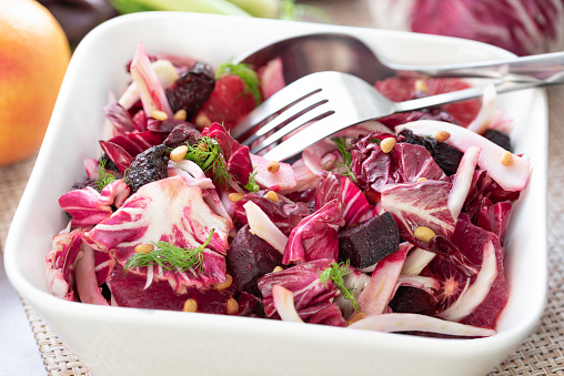 Homemade mixed roasted beet salad with radicchio, blood oranges, sliced fennel, roasted pine nuts, garnish with fennel fronds and drizzle with a vinaigrette in a white salad bowl for one delicious winter salad