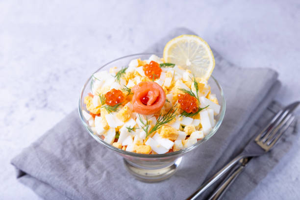 Puff salad with salted trout (salmon), caviar, egg and vegetables. A traditional dish. One serving in a glass glass on a gray background. Large n