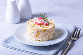 Crab salad with corn and boiled eggs on a white plate. Serving for one person. Traditional Russian salad. Selective focus,