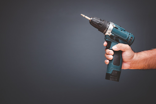 Blue Battery Screwdriver or Drill in Male Hands Over Gray Background, Copy Space.