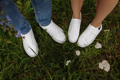 Legs of a man and a woman in white sneakers on green grass. View from above.