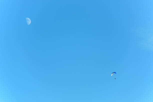 Paramotor in flight on a sunny day with the moon in the sky. France.