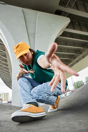 Fisheye of young Asian man dancing outdoors and gesturing to camera wearing colorful street style clothes