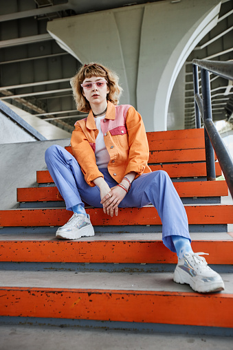 Vertical portrait of young carefree woman wearing colorful street style fashion outdoors in urban setting