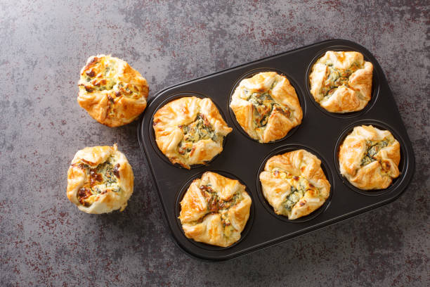 muffin di pasta sfoglia al formaggio feta fatti in casa con primo piano di spinaci nella padella di maffin. vista orizzontale dall'alto - bun bread cake dinner foto e immagini stock