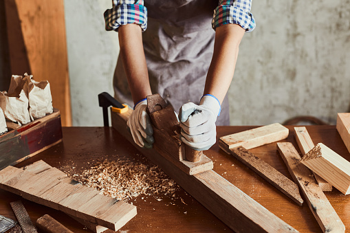 Female hand Planing Wood In Carpentry Workshop. Carpenter woman working with plane. Girl working with equipment on a wooden table.