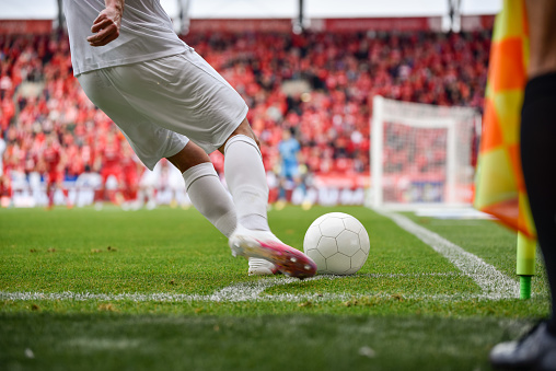 Footballer takes the corner. Detail of player's legs and the ball during soccer match.