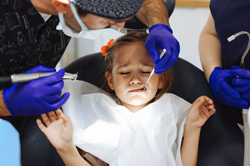 Shot of a young little girl lying down on a dentist chair while getting a checkup from the dentist