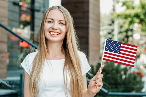微笑みながら小さなアメリカ国旗を見せ、大学の背景に立つ女子学生 - university symbol built structure independence ストックフォトと画像