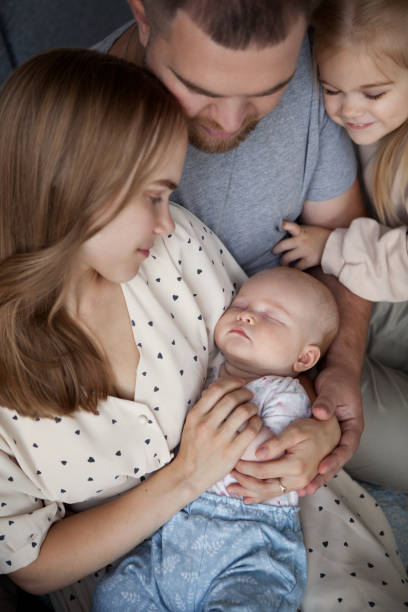 Close up of family with two children looking at newborn sleeping baby in mom's arms stock photo