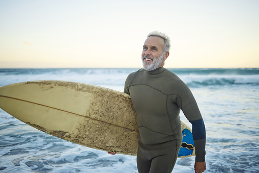 Water, happy and man surfing at the beach on a tropical holiday in Hawaii during sunrise in summer. Mature surfer with smile for the waves in ocean on vacation on an island for travel and adventure