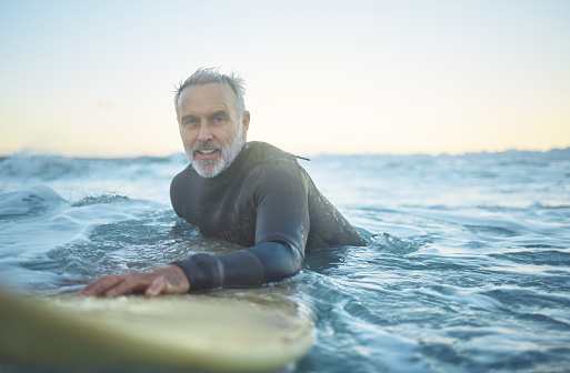 Senior man, surfing in the ocean of Indonesia and free to travel the world in retirement life. Retired surfer, swimming in the sea for fitness and exercise looking to catch a perfect wave on holiday