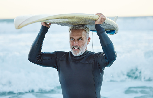 Senior man, ocean surfer and carrying surfboard on holiday, vacation or summer trip in Canada. Workout, fitness and retired male with board after surfing, water sports and training exercise by sea.