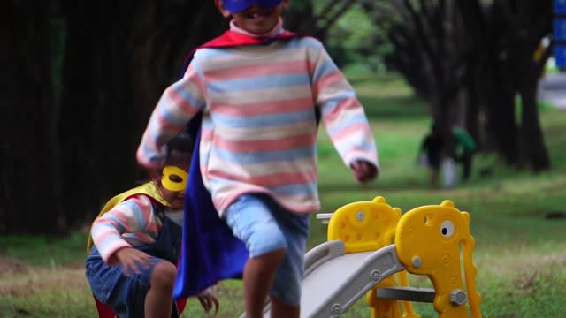 Children wearing masks and capes playing in the park.