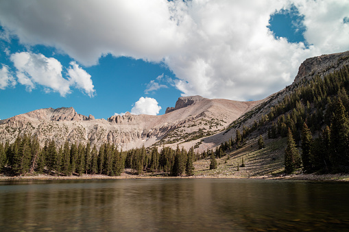 Stella Lake, an alpine lake located within Great Basin National Park in Nevada seen on a summer day. Wheeler Peak is visible in the background. The sky is filled with white cumulus clouds.
