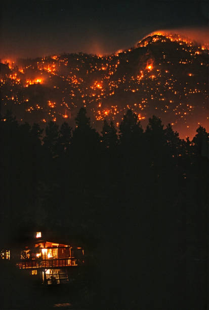 Glowing in the night like a volcano with stars overhead, the wind blows smoke and hot spots during a man made forest fire burning out of control on a mountain hillside through pine trees above a Rocky Mountain log home and highway 285 near the small town of Bailey, Colorado on April 23, 2002.