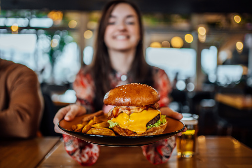 Young cheerful woman holding a plate with a tasty burger at a restaurant