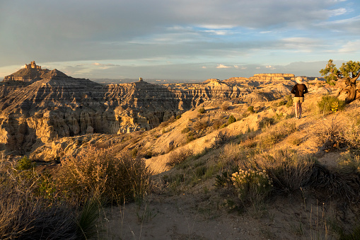 Standing at an overlook, a woman watches the sunset over Angel Peak and the desert landscape of sandstone rock spires and canyons in the New Mexico badlands of the Angel Peak National Recreation Area.