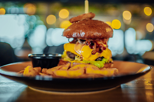 Burger in bun with cheese and vegetable garnish, served with French fries on pub table