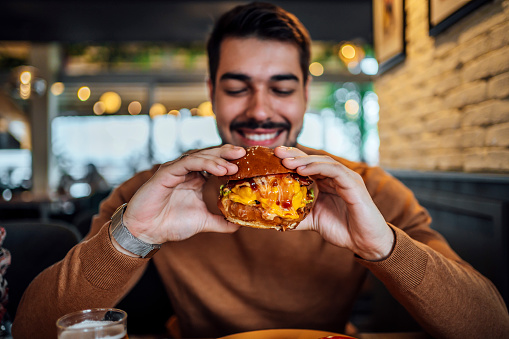 Young smiling hungry man ready to eat a burger at a restaurant